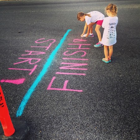 Two young girls mark a start/finish line, using bright pink spray paint, Logan, United States. Photo by Aw Creative for Unsplash.